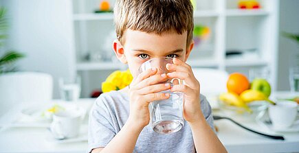 Kind trinkt ein Glas Wasser am Frühstückstisch.