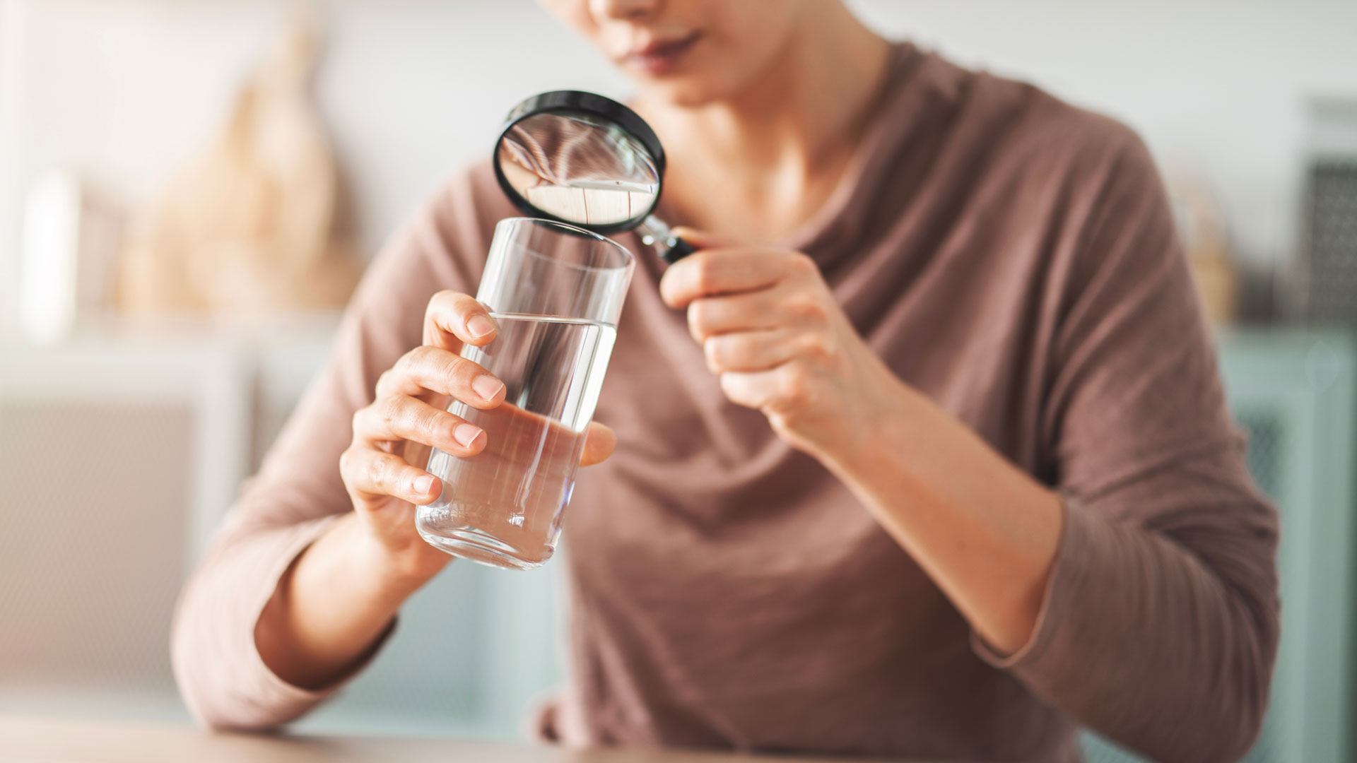 Trinkwasserlabor: Analyse und Qualitätsprüfung von Wasser bei GANZIMMUN Trinkwasserlabor – Frau untersucht ein Glas Wasser mit Lupe zur Qualitätskontrolle